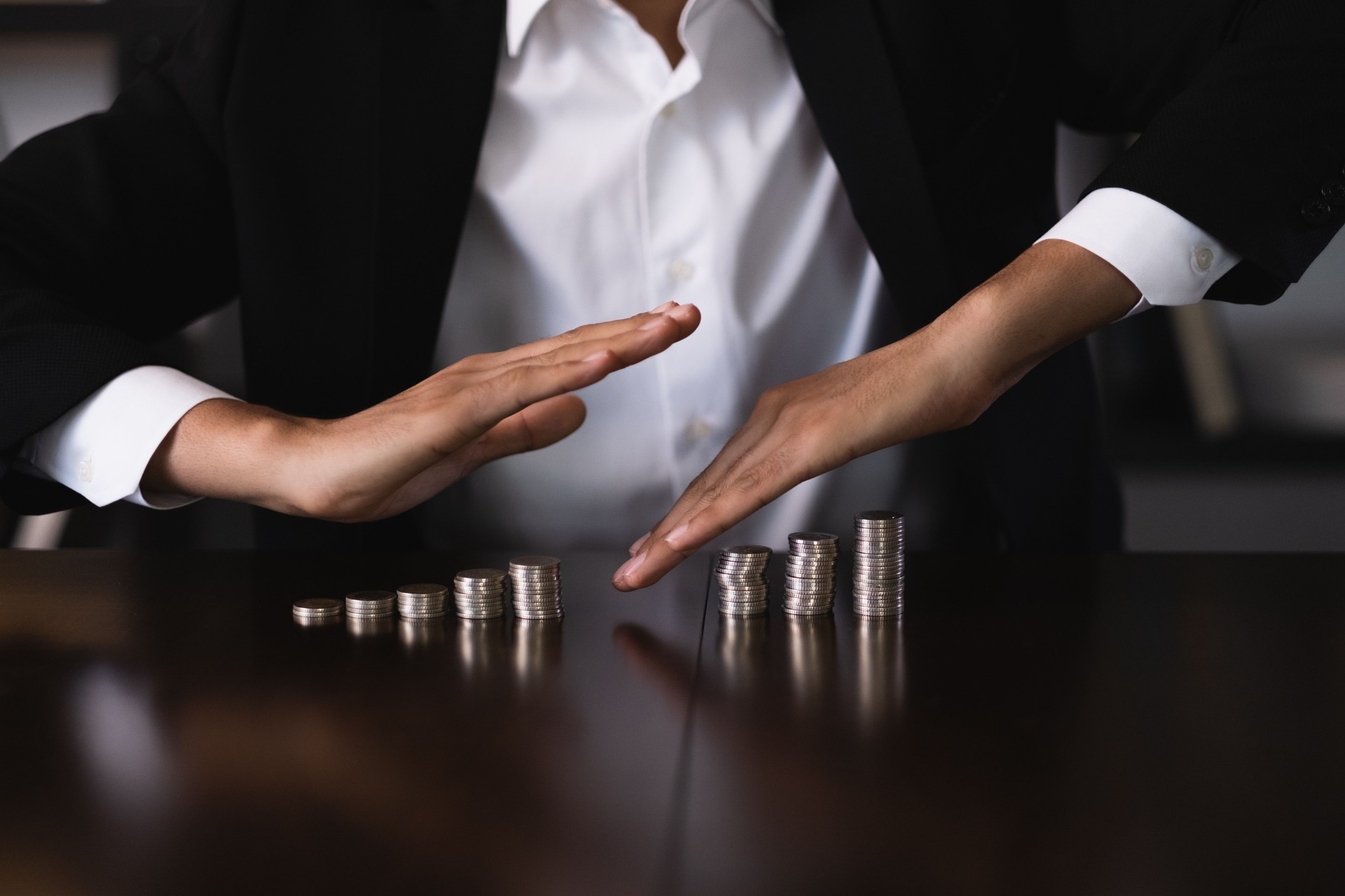 Businessman protecting increasing stacks of coins on desk